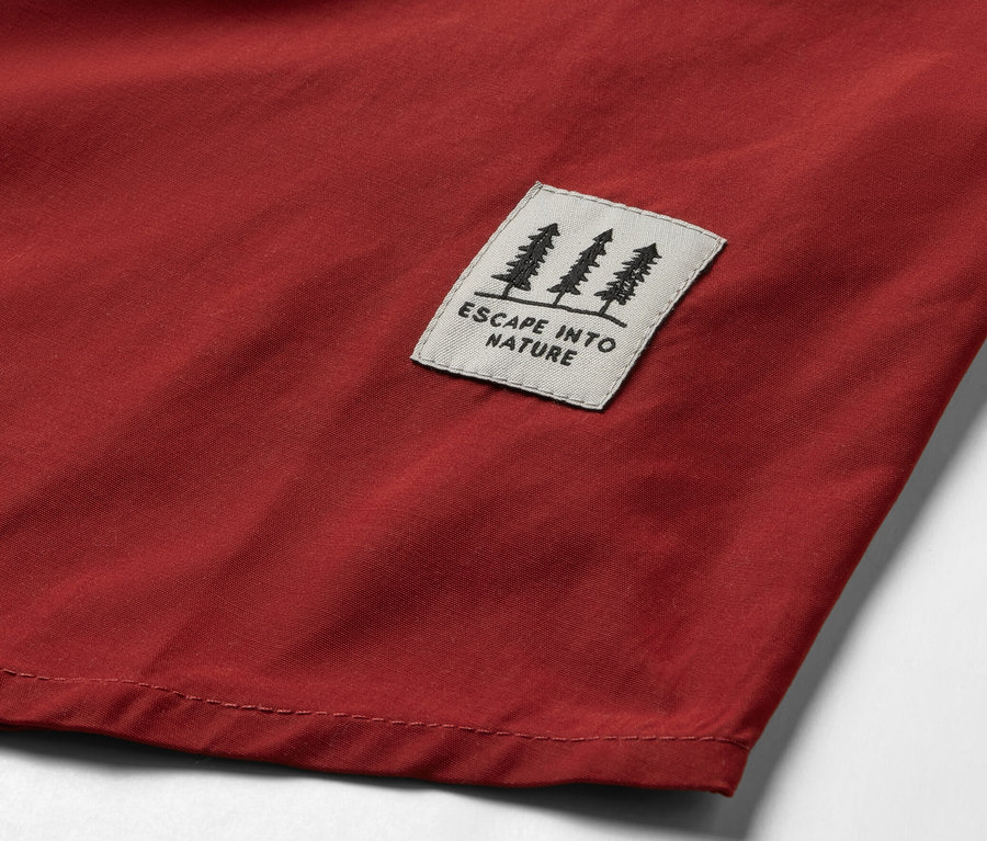 Détail d’une blouse d’extérieur rouge avec un patch représentant des arbres et l’inscription « ESCAPE INTO NATURE ».