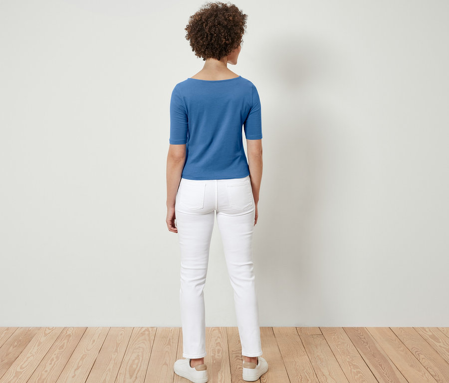 Une femme se tient dos à la caméra et porte un t-shirt bleu à manches courtes.