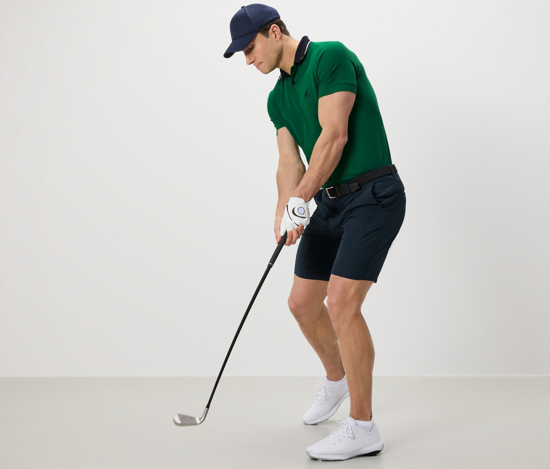 Homme en polo vert et short fonctionnel jouant au golf.