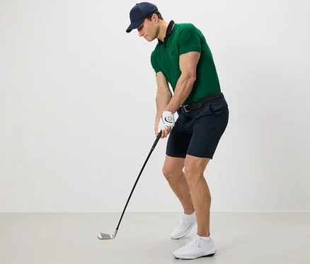 Homme en polo vert et short fonctionnel jouant au golf.