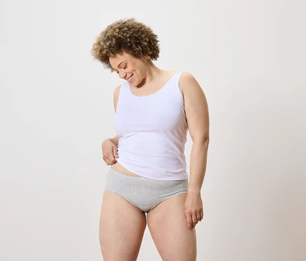 Une femme aux cheveux bouclés porte un débardeur blanc et une culotte à rayures grises et regarde vers le bas.