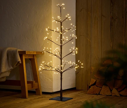 Un arbre décoratif avec des lumières blanches chaudes se dresse sur un plancher en bois à côté d'un banc.