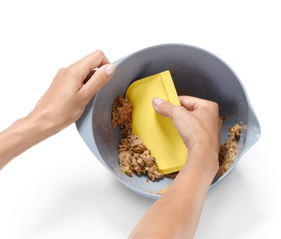 Une paire de mains mélange de la pâte dans un bol avec une spatule jaune.
