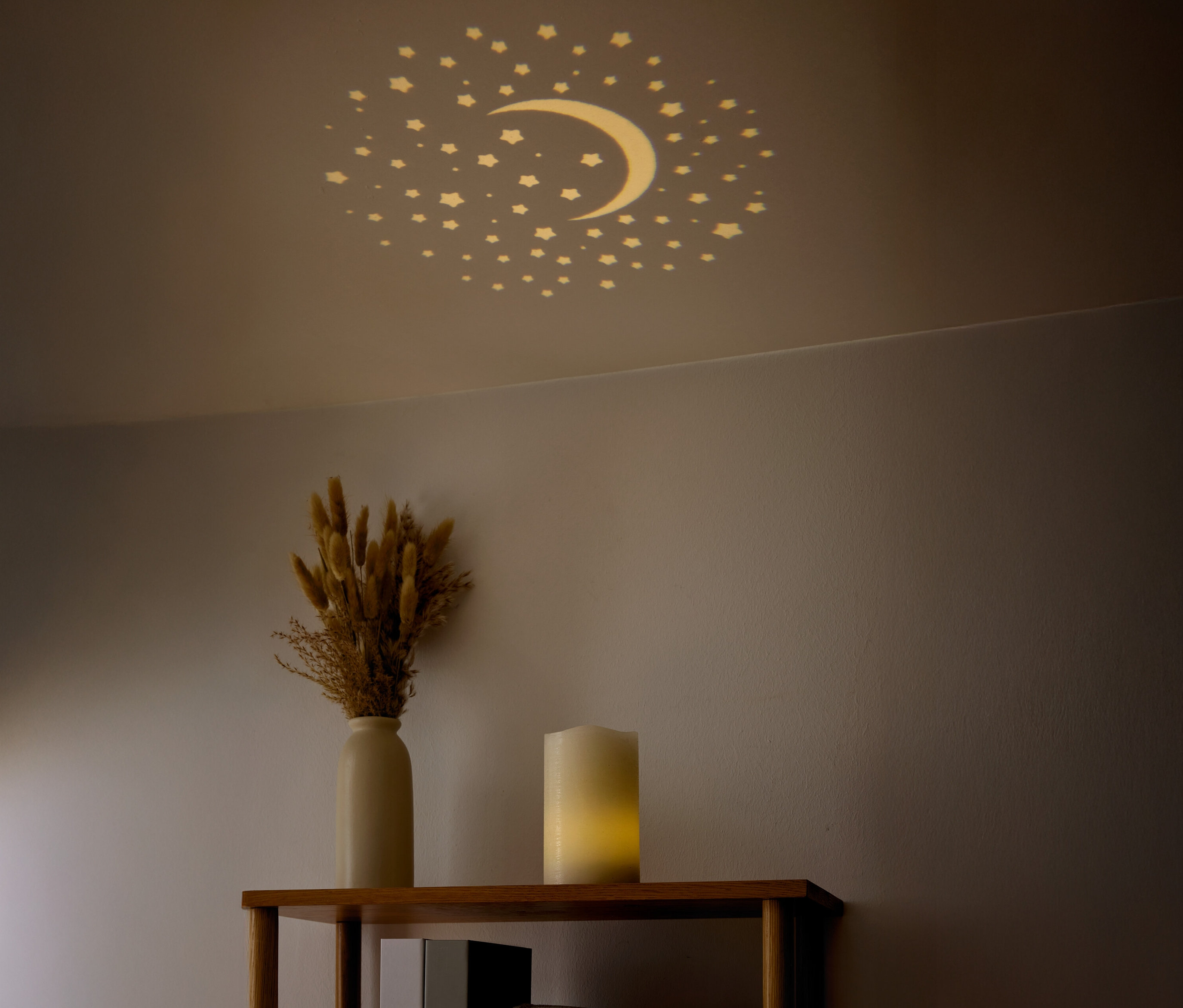 Des étoiles et un croissant de lune sont visibles au plafond. Un vase avec des fleurs séchées et une bougie sont posés sur une étagère.