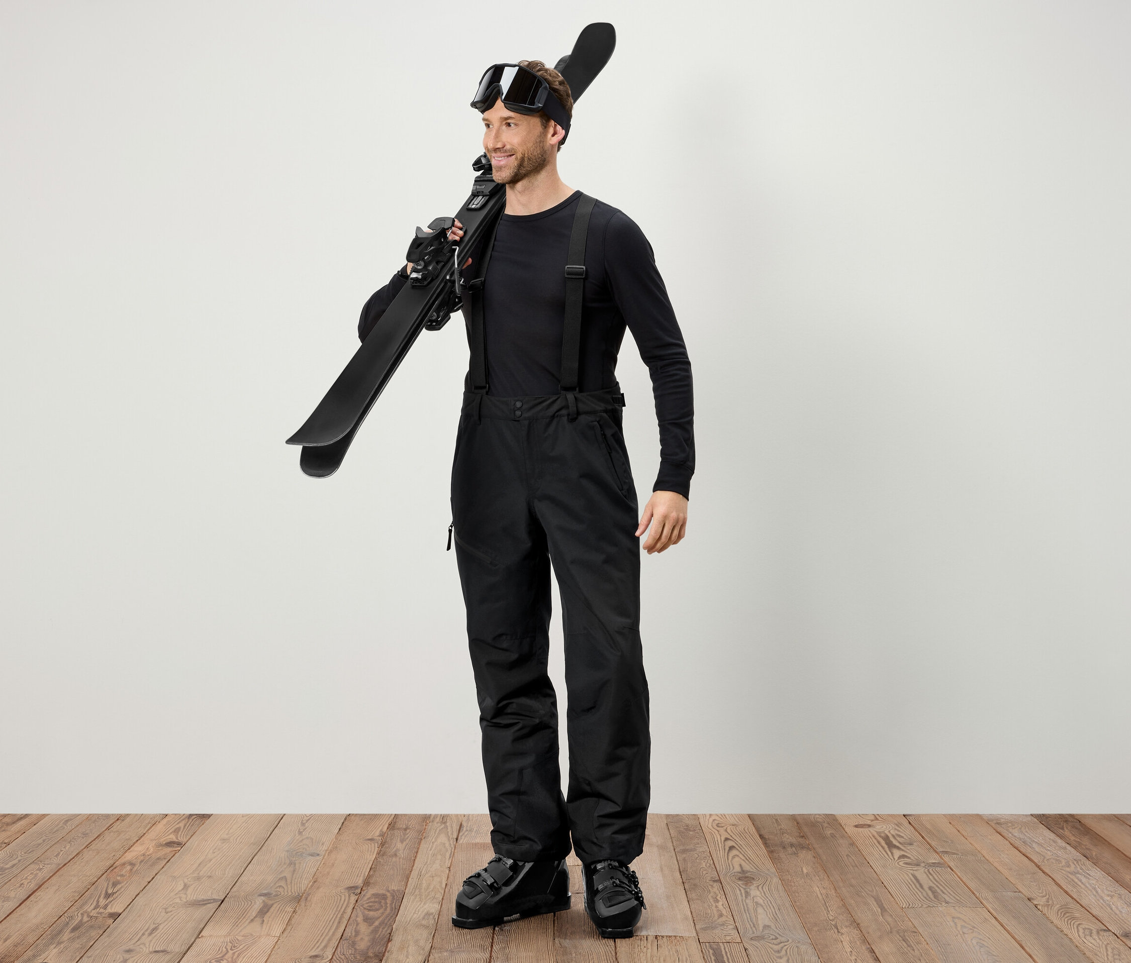 Un homme en tenue de ski noire porte des skis sur l'épaule.