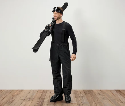 Un homme en tenue de ski noire porte des skis sur l'épaule.