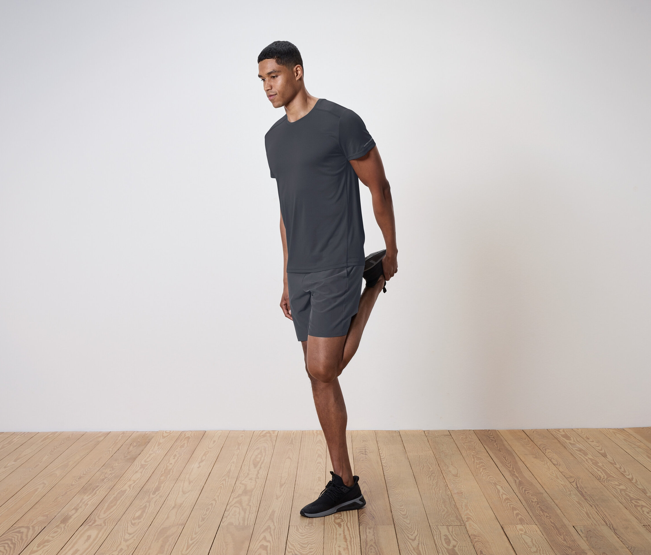 Un homme étire son quadriceps sur un fond de mur blanc.