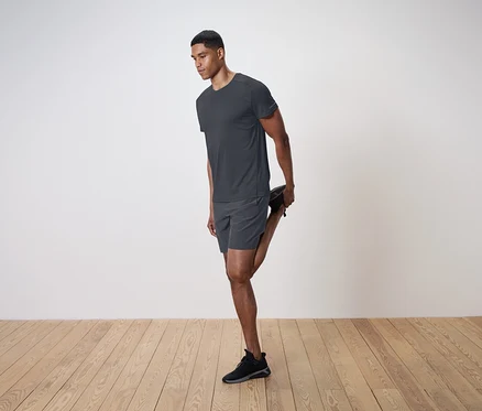 Un homme étire son quadriceps sur un fond de mur blanc.