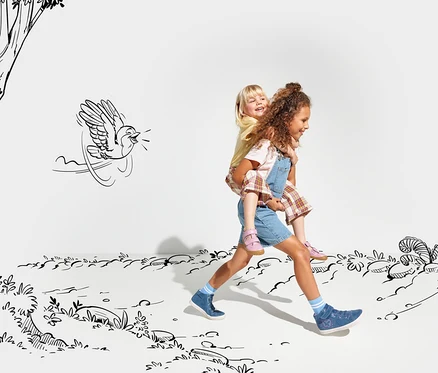 Une fille porte un garçon sur son dos et ils marchent tous les deux dans un paysage dessiné. La fille porte une robe en jean et des sandales roses Lurchi « Barefoot ». Le garçon porte un t-shirt jaune et un short à carreaux.