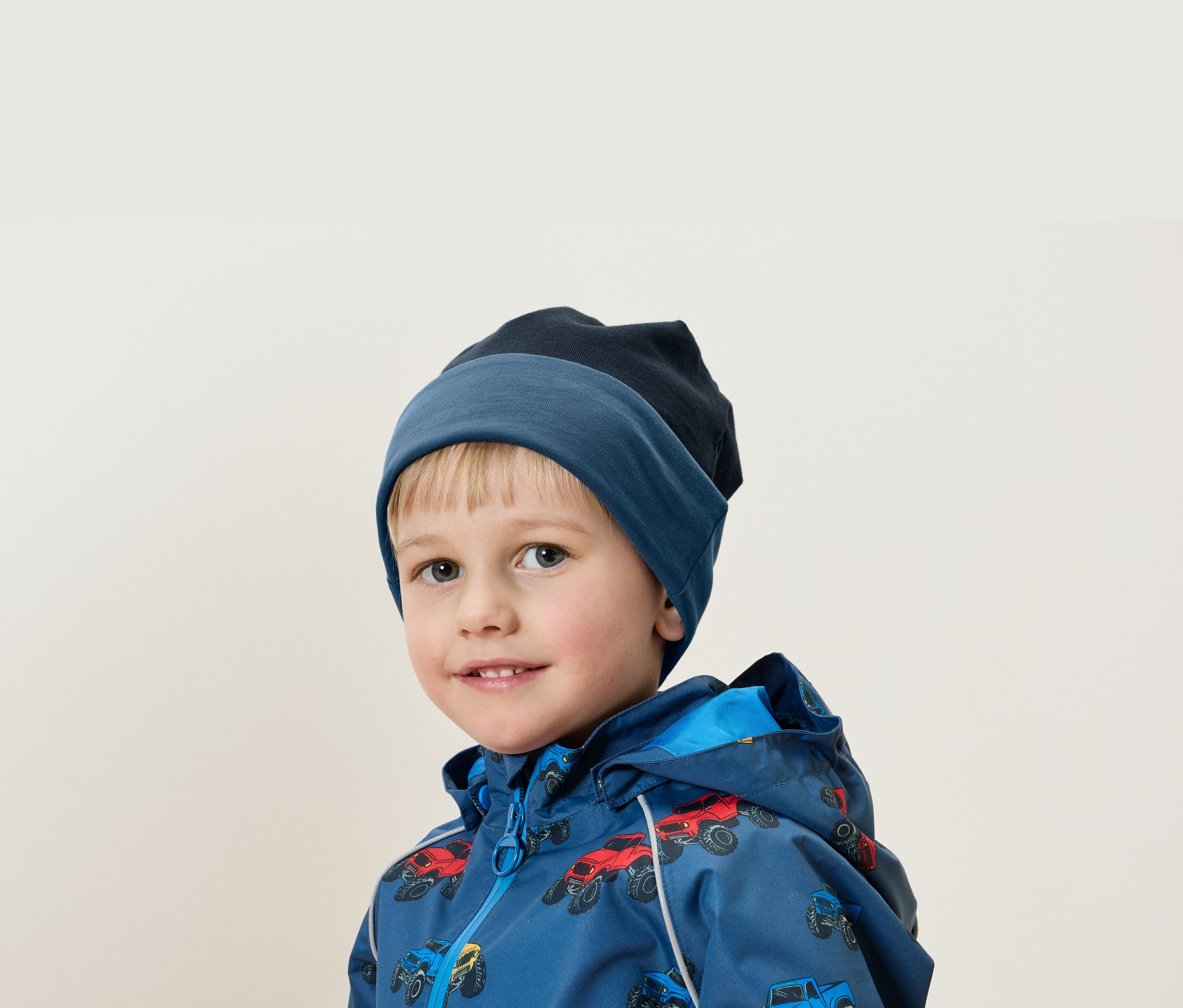 Portrait d'un garçon blond portant un bonnet bleu et une veste à imprimé de voitures.