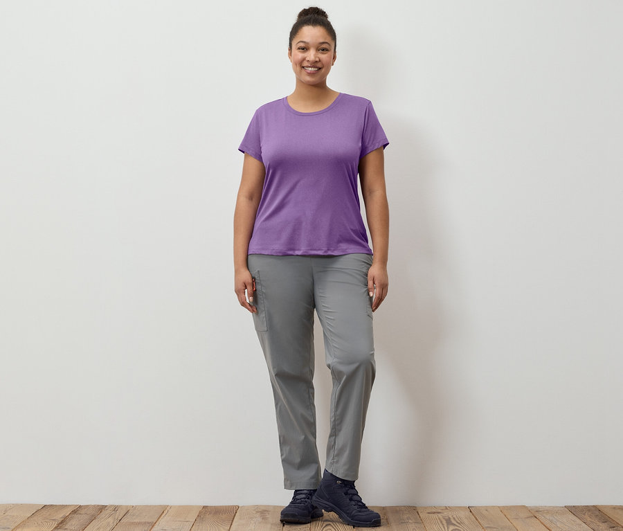 Une femme debout portant un pantalon outdoor pliable gris et un t-shirt fonctionnel extensible.