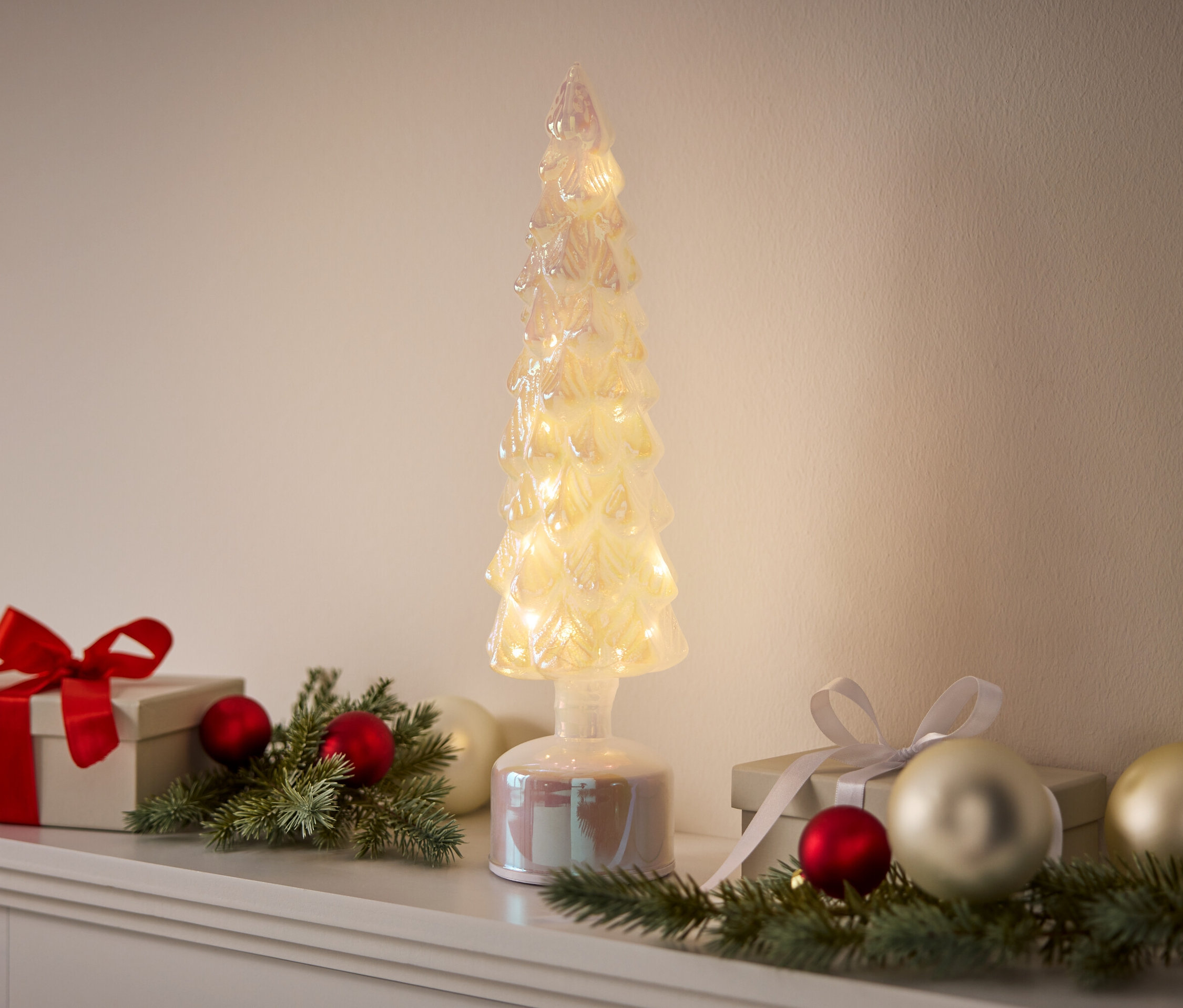 Un arbre décoratif illuminé se dresse entre des cadeaux et des décorations.