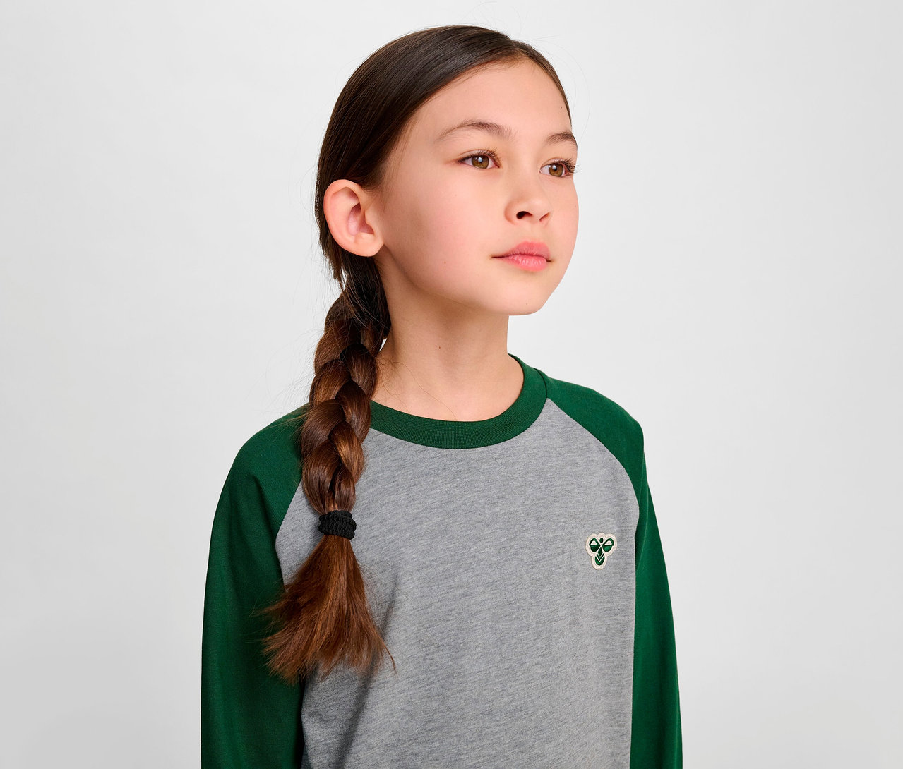 Fillette avec une tresse portant un t-shirt ample à manches raglan HUMMEL HMLJR BEE vert.