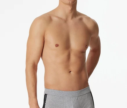 Un homme pose torse nu en portant un short SCHIESSER gris chiné avec une bande noire sur le côté.