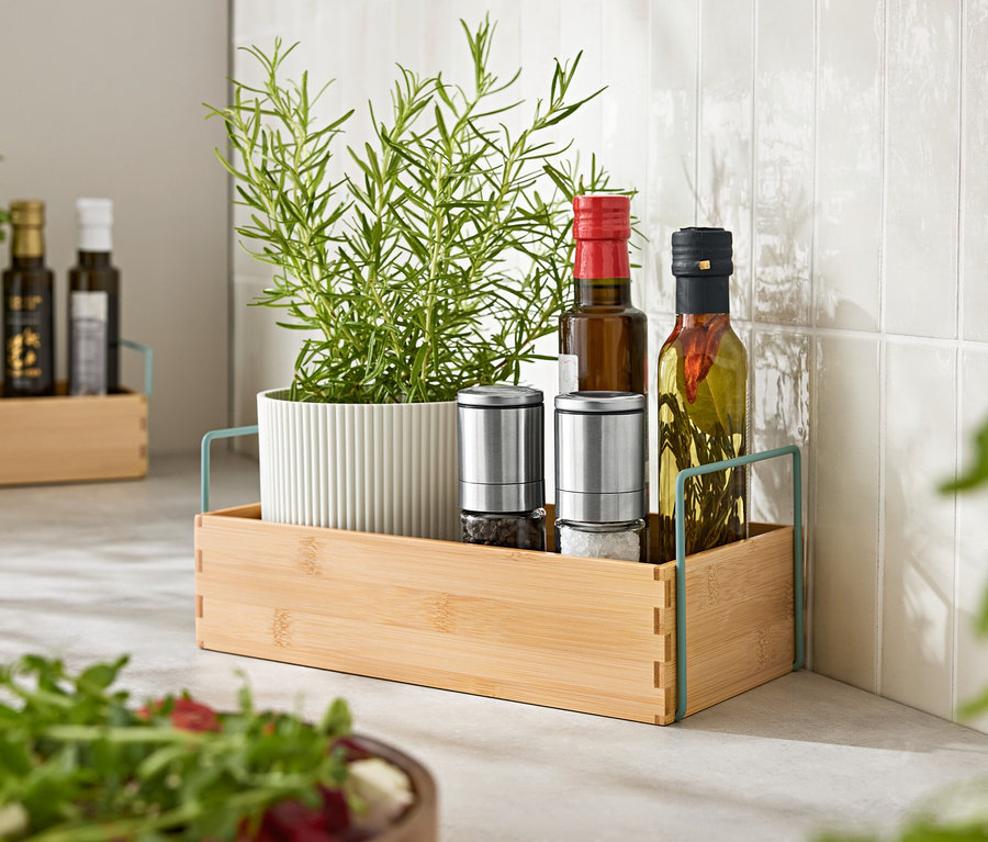 Herbes en pot, deux moulins à épices et deux bouteilles d'huile dans un plateau en bois.