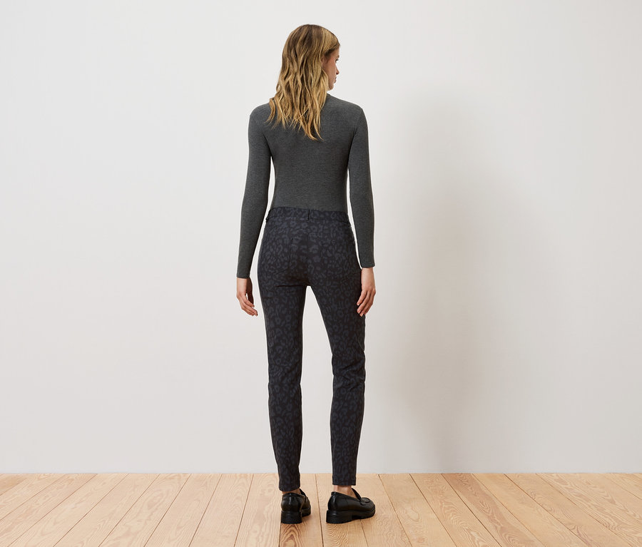 Une femme, vue de dos, porte un haut gris à manches longues et un pantalon noir à motifs.
