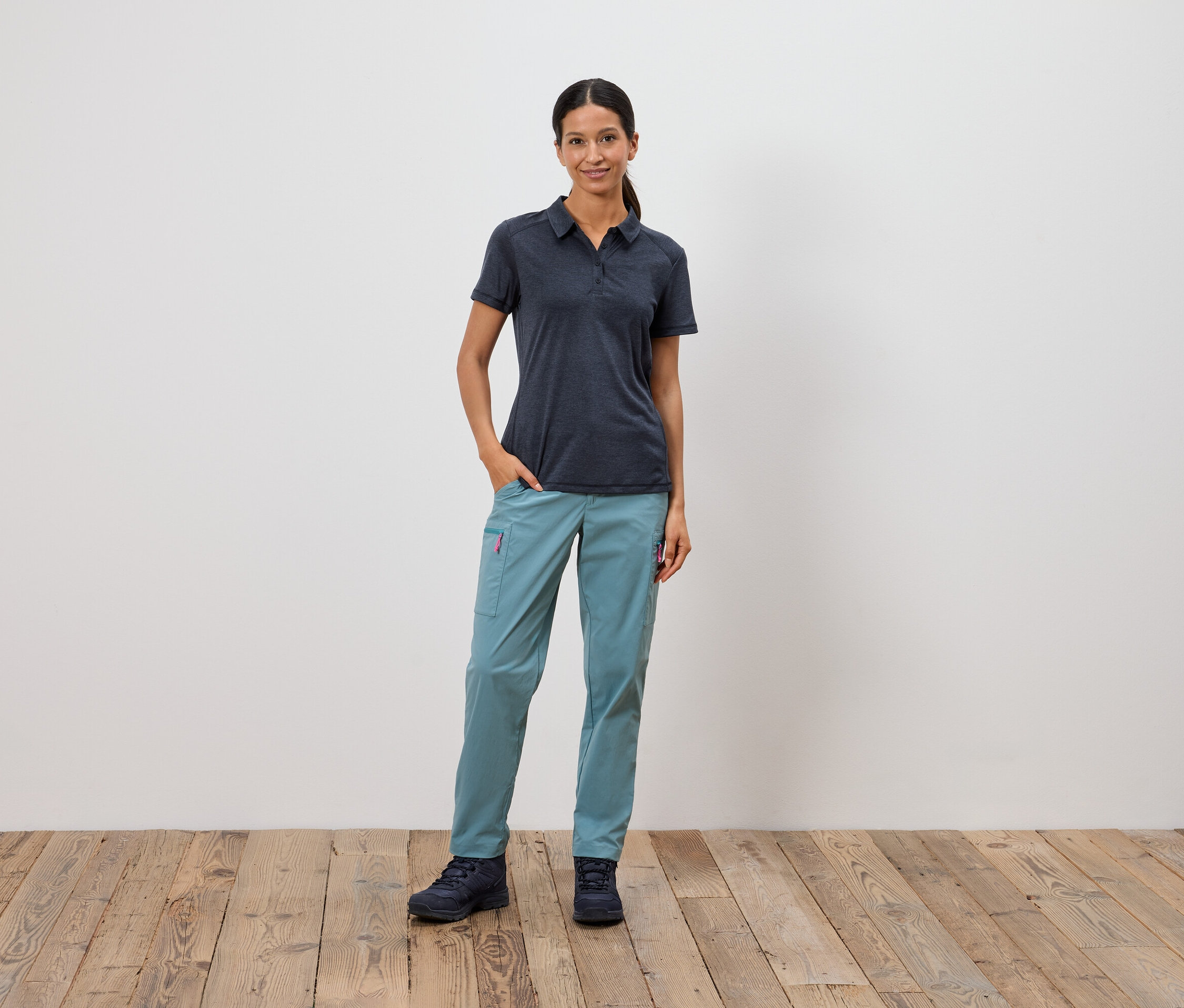 Une femme se tient debout, une main dans la poche, devant un mur blanc.