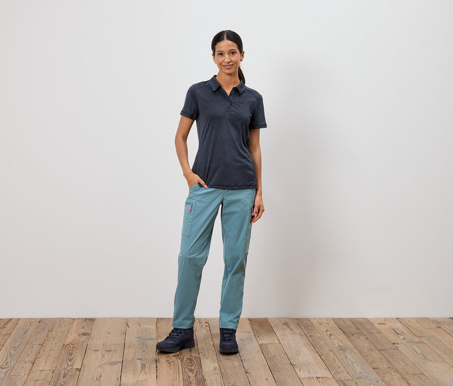 Une femme se tient debout, une main dans la poche, devant un mur blanc.