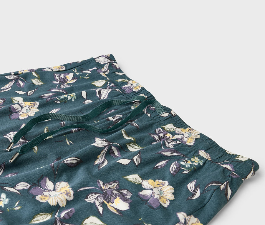 Gros plan d'un pantalon vert foncé avec un motif floral et un cordon de serrage vert.