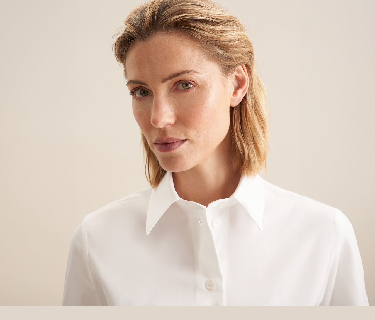 Femme aux cheveux blonds portant un chemisier blanc à manches courtes Seidensticker, regardant vers l'avant.