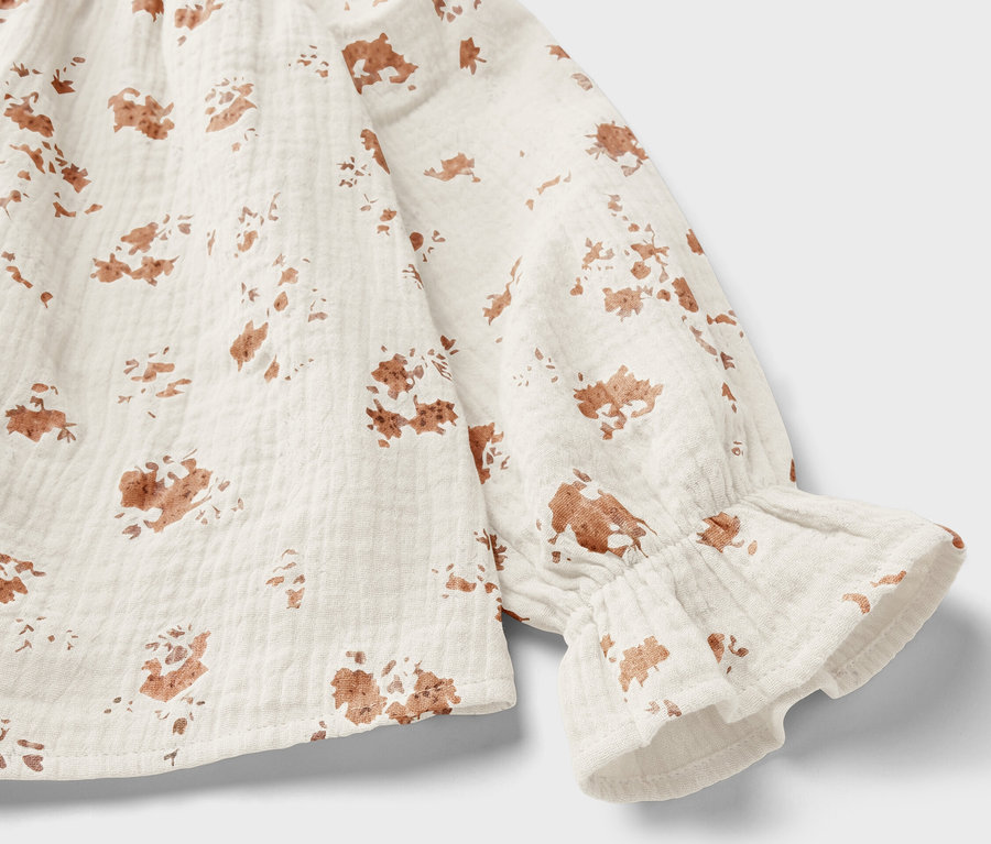 Gros plan sur une blouse en mousseline pour enfant avec un motif floral marron et des volants sur la manche.