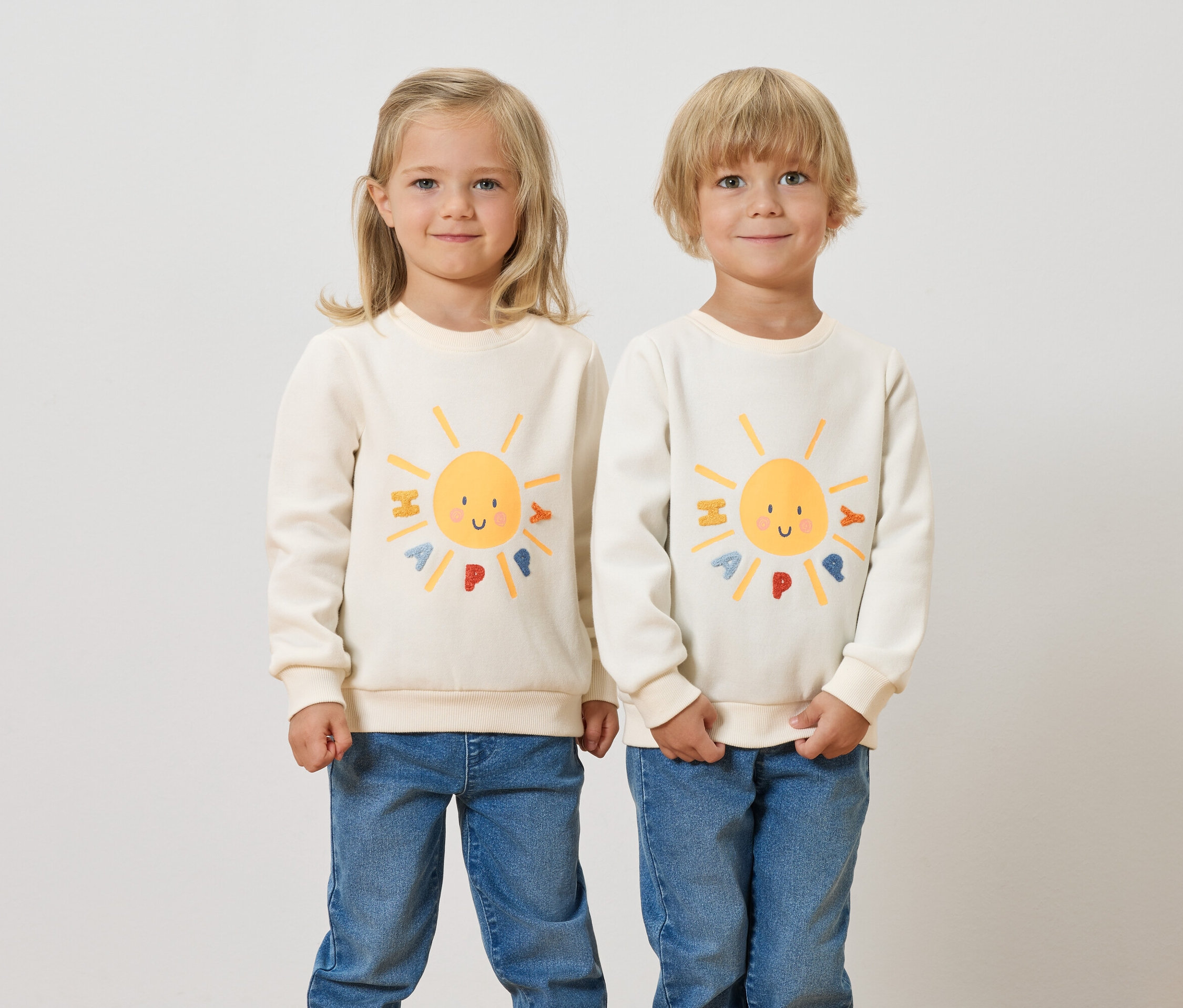 Deux enfants se tiennent côte à côte et portent des sweatshirts pour enfants avec un intérieur gratté et un motif de soleil.