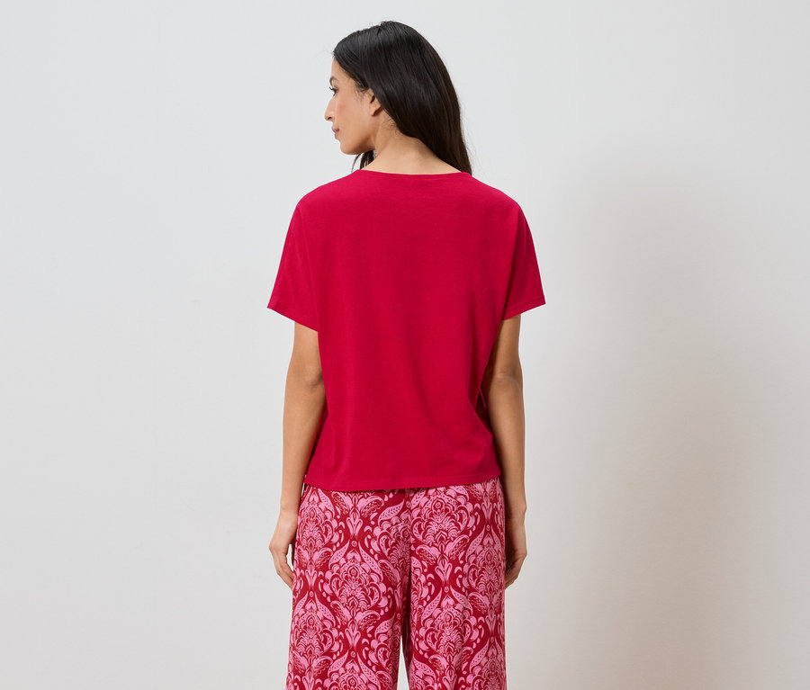 Vue arrière d'une femme aux cheveux foncés portant un t-shirt rouge et un pantalon rose à motifs.