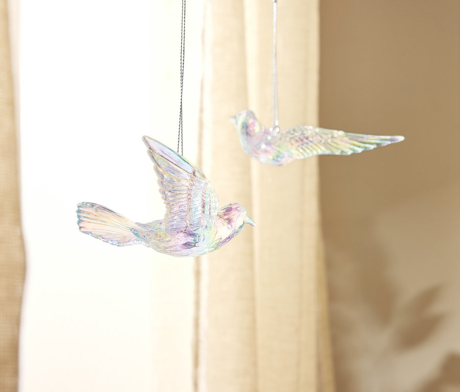 Deux décorations d'oiseaux scintillantes suspendues devant un rideau beige.