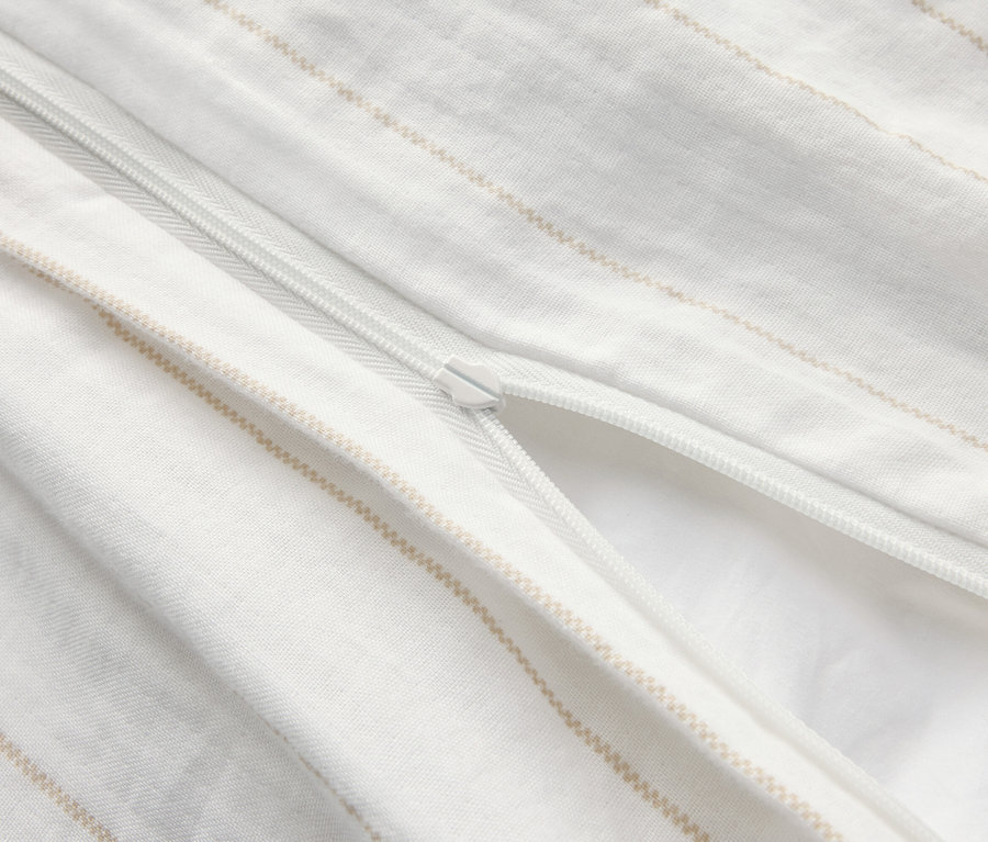 Gros plan d'une housse de couette blanche partiellement ouverte avec un motif à rayures beiges et une fermeture éclair.