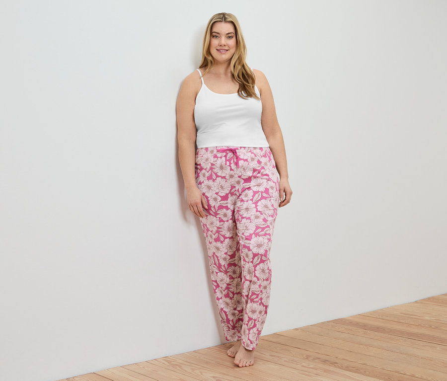 Femme appuyée contre un mur, portant un 2 Hemdchen blanc et un pantalon rose à fleurs.