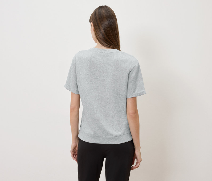 Vue de dos d'une femme aux longs cheveux bruns portant un t-shirt gris et un pantalon noir.