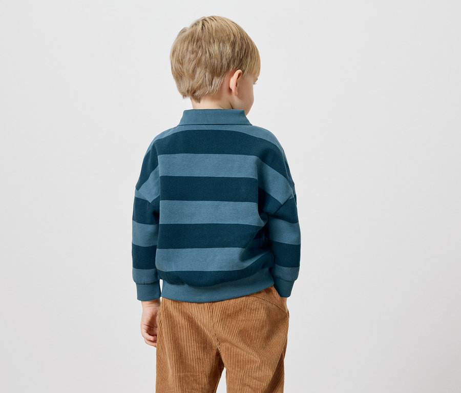 Vue arrière d'un enfant blond portant un haut à manches longues rayé bleu et un pantalon en velours côtelé marron.