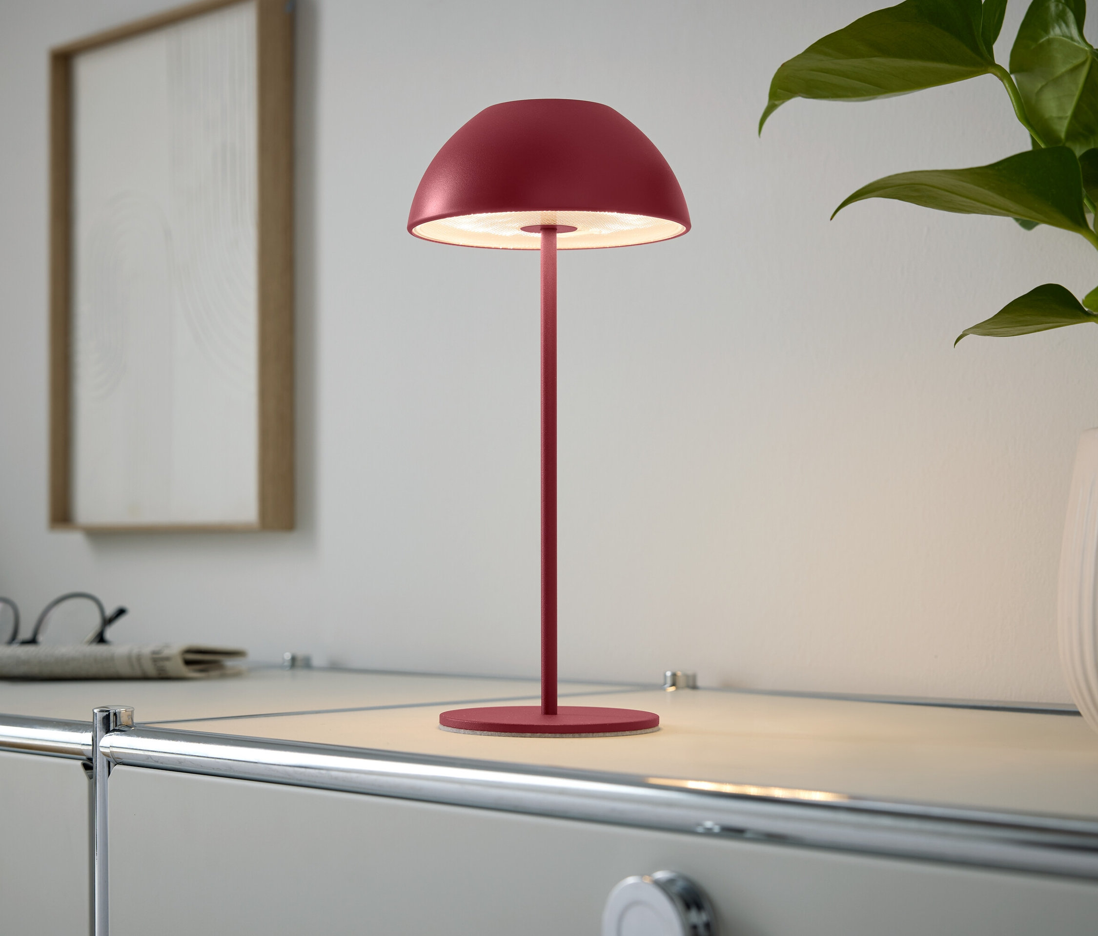 Une lampe rouge est posée sur une armoire à côté d'une plante d'intérieur.