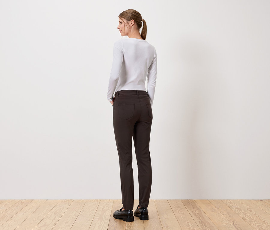 Une femme se tient dos à la caméra, portant un pantalon long et un haut à manches longues.