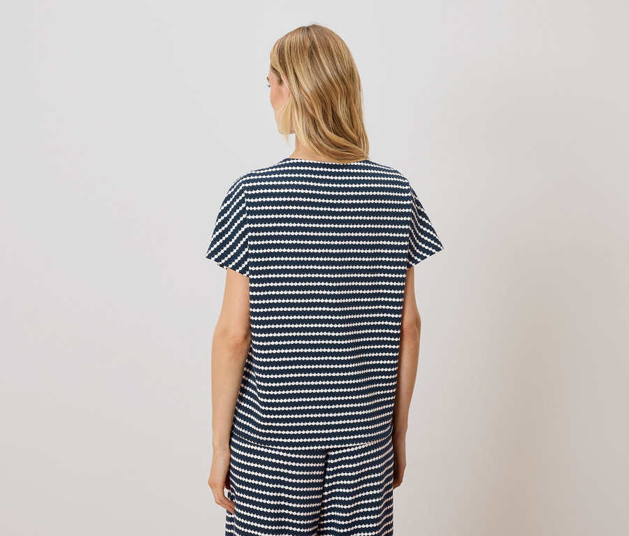 Une femme blonde porte un haut à manches courtes rayé bleu marine et blanc et un short.