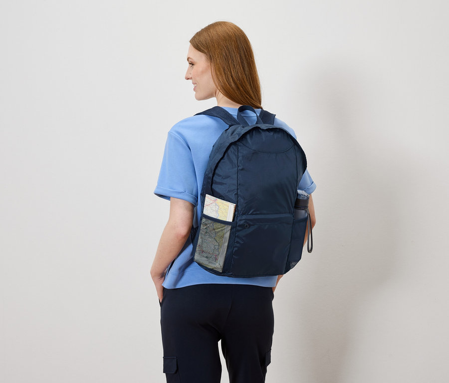 Femme vue de dos avec un sac à dos bleu marine contenant une carte et une bouteille d'eau.
