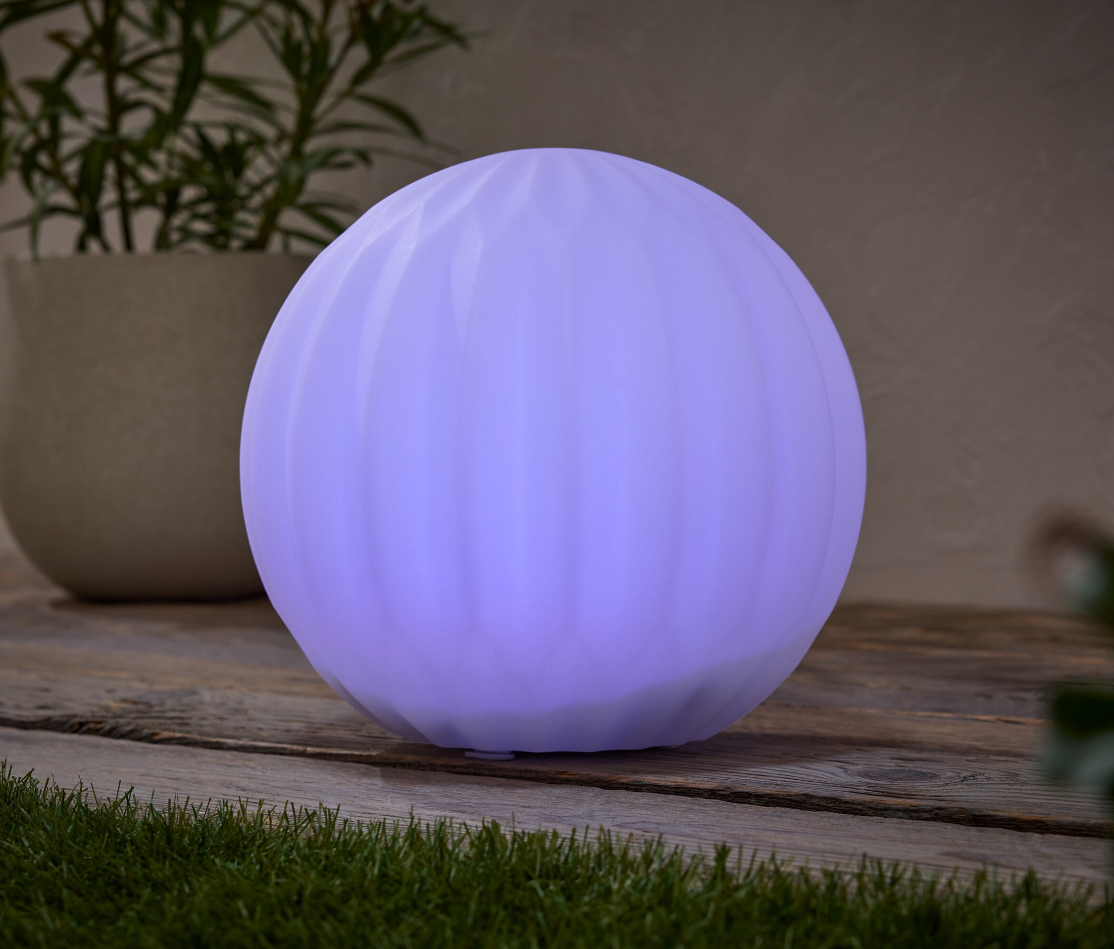 Une lampe ronde violette est posée sur une table en bois, à côté d'une plante en pot.