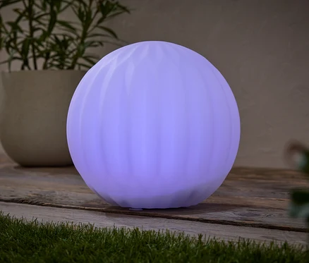 Une lampe ronde violette est posée sur une table en bois, à côté d'une plante en pot.
