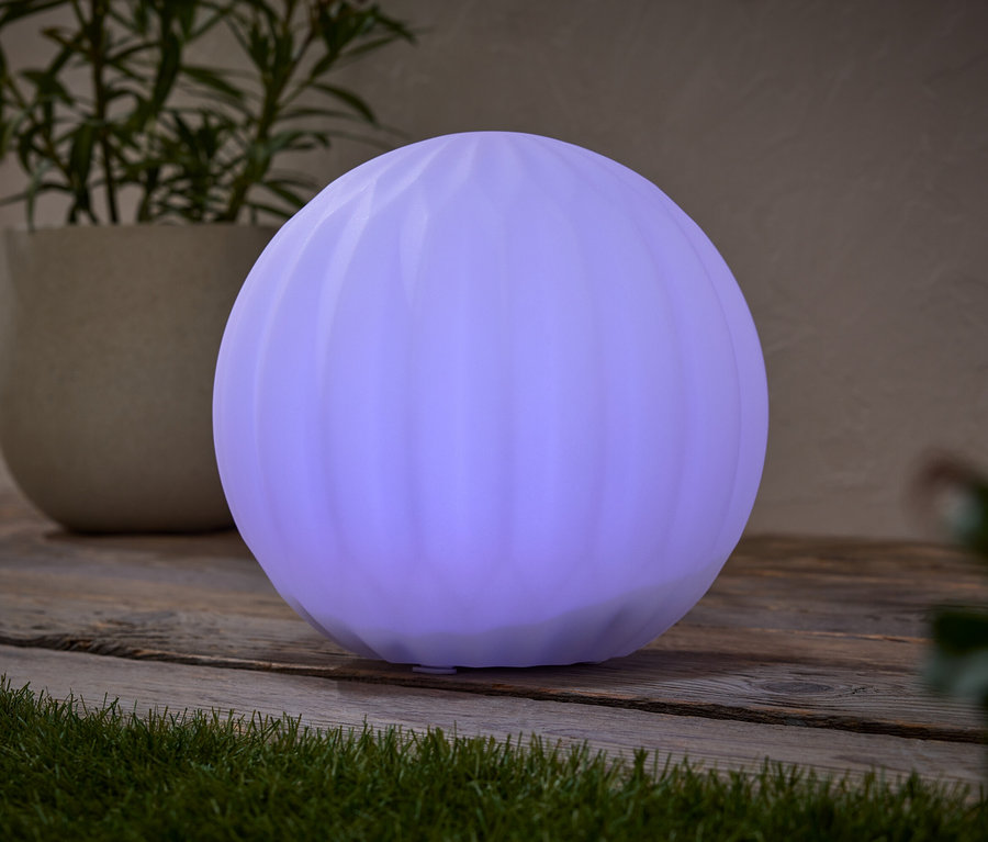 Une lampe ronde violette est posée sur une table en bois, à côté d'une plante en pot.