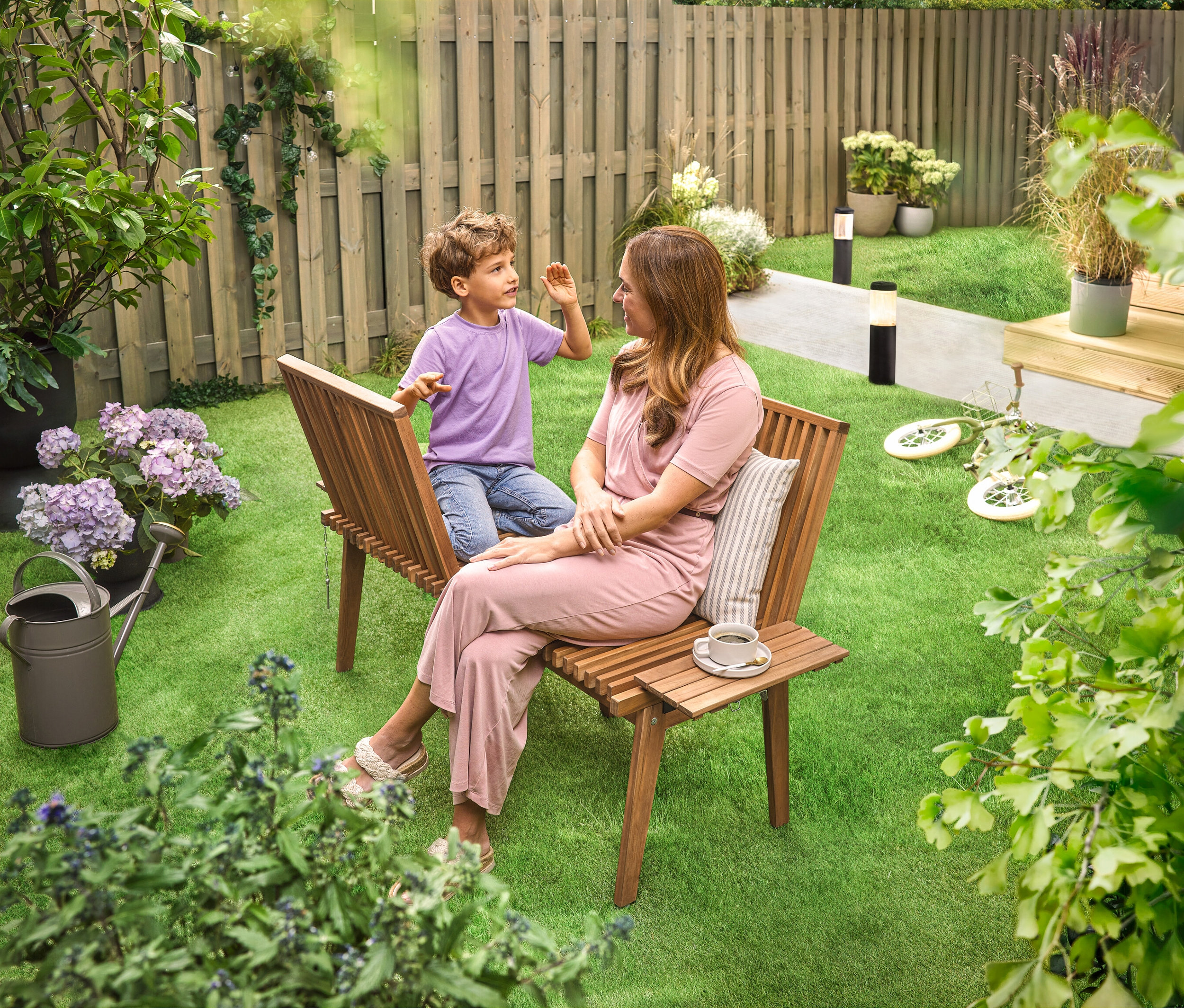 Une femme est assise avec un enfant sur une banque de discussion flexible dans le jardin. À l'arrière-plan, on peut voir 2 lampes solaires de chemin striées.