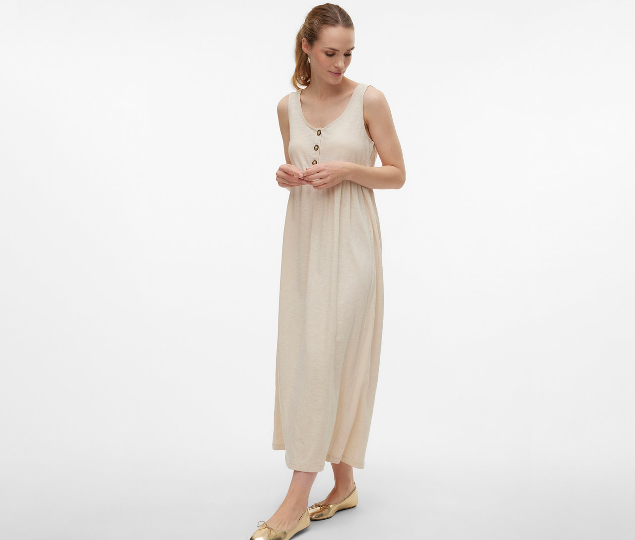 Femme portant une robe de grossesse MAMALICIOUS «
MLEVI LIA » avec des boutons et des ballerines dorées sur fond blanc.