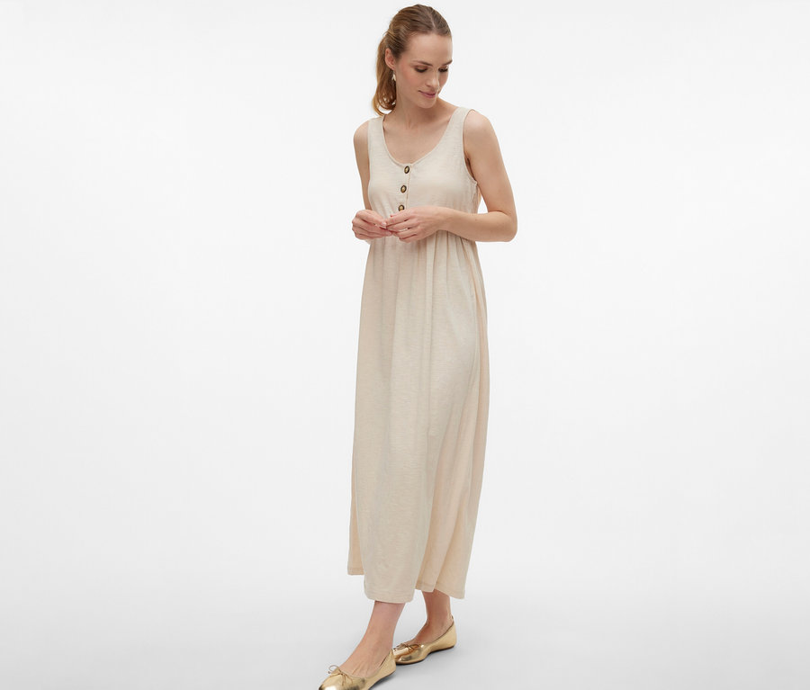 Femme portant une robe de grossesse MAMALICIOUS «
MLEVI LIA » avec des boutons et des ballerines dorées sur fond blanc.
