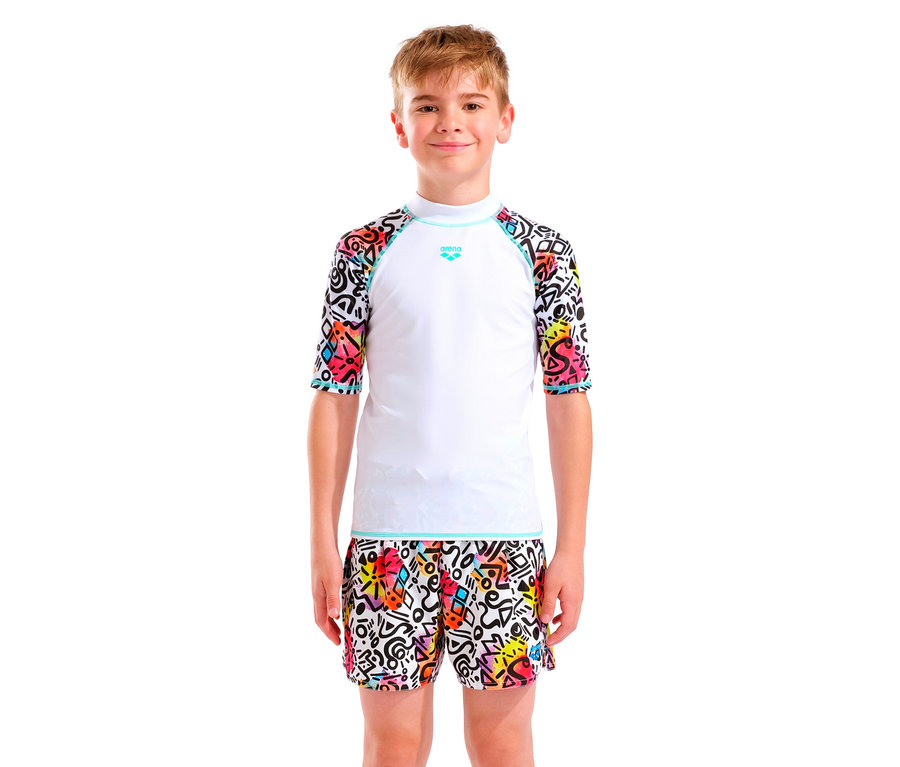 Un garçon aux cheveux blonds porte un haut Arena blanc avec des manches colorées et un short assorti.