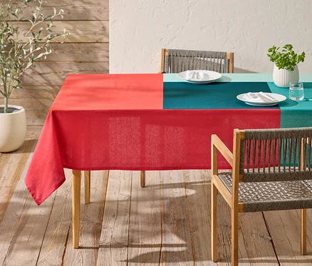 Une table avec une nappe à carreaux rouge et turquoise et deux chaises se trouve sur une terrasse en bois.