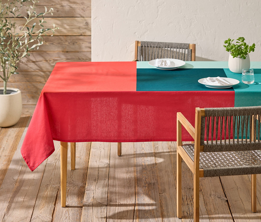Une table avec une nappe à carreaux rouge et turquoise et deux chaises se trouve sur une terrasse en bois.