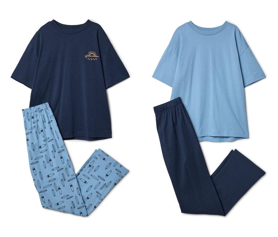 Deux pyjamas à manches courtes pour enfant sont posés à plat. À gauche, un haut bleu foncé avec un motif de soleil et de vagues, et un pantalon bleu clair avec un motif de planches de surf. À droite, un haut bleu clair et un pantalon bleu foncé.