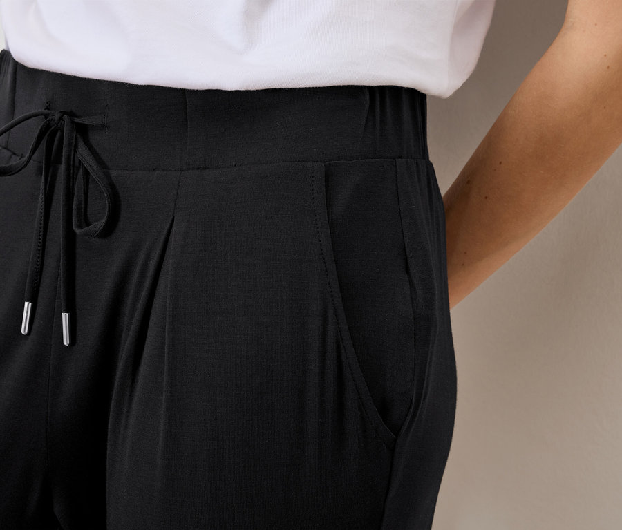 Gros plan d'une femme portant un pantalon noir ample avec cordon de serrage et poches.
