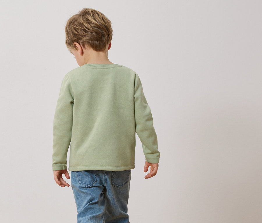 Un enfant de dos, portant un pull vert clair et un jean.