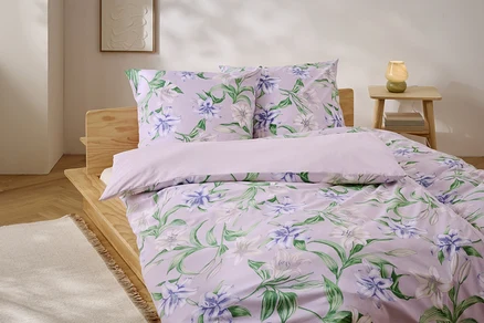 Lit avec des draps lilas à motif floral et un cadre de lit en bois.