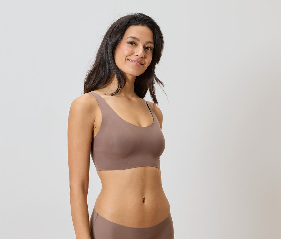 Femme portant un ensemble de sous-vêtements marron sur un fond neutre.